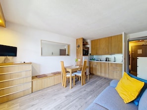 A compact living space with a dining area, kitchenette, and a sofa with a yellow pillow.