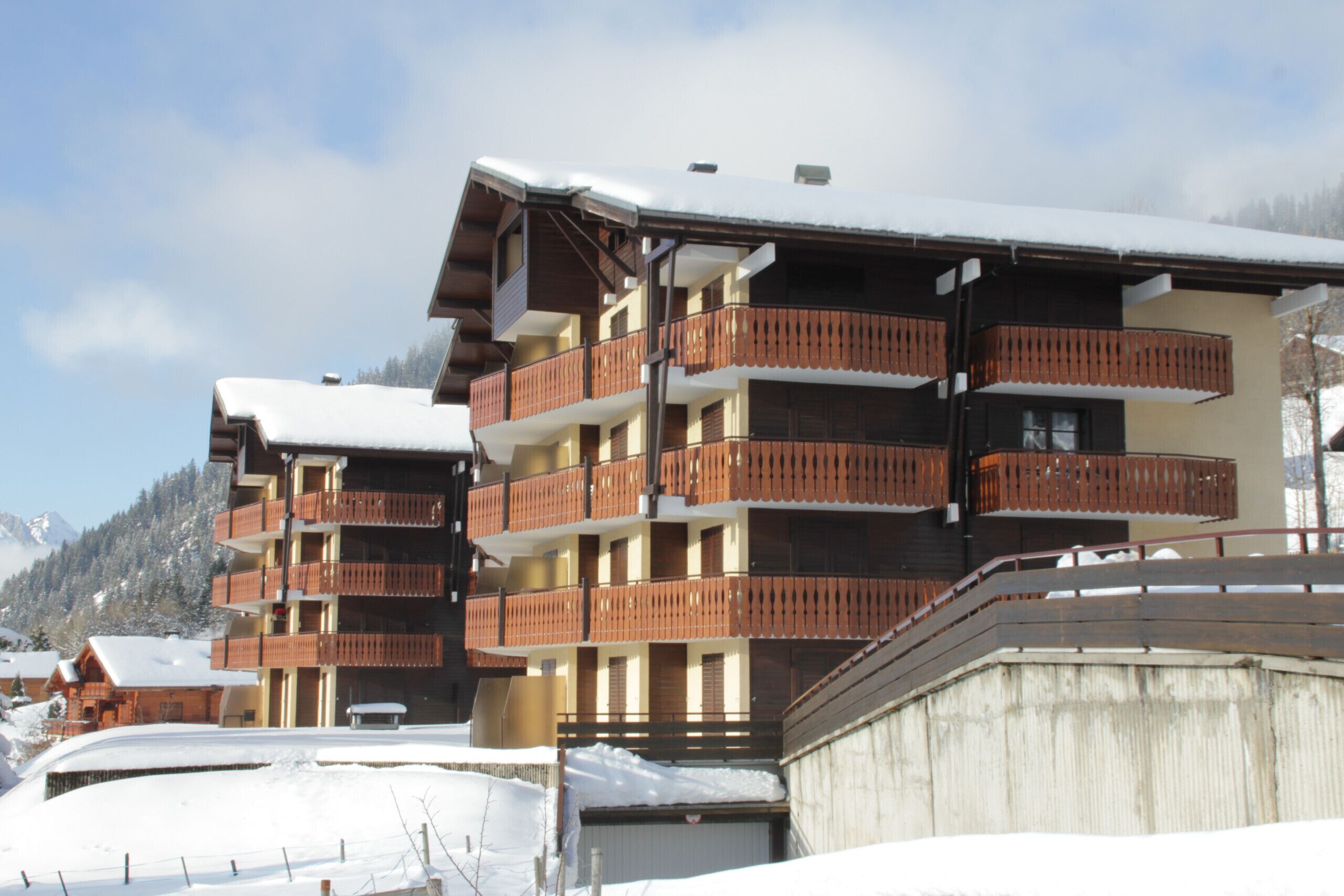 A multi-story hotel with balconies, snow-covered roofs, and a mountainous backdrop.