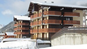A multi-story hotel with balconies, snow-covered roofs, and a mountainous backdrop.