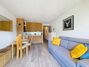 A modern living space with a dining area, kitchen, and a sofa with yellow cushions.