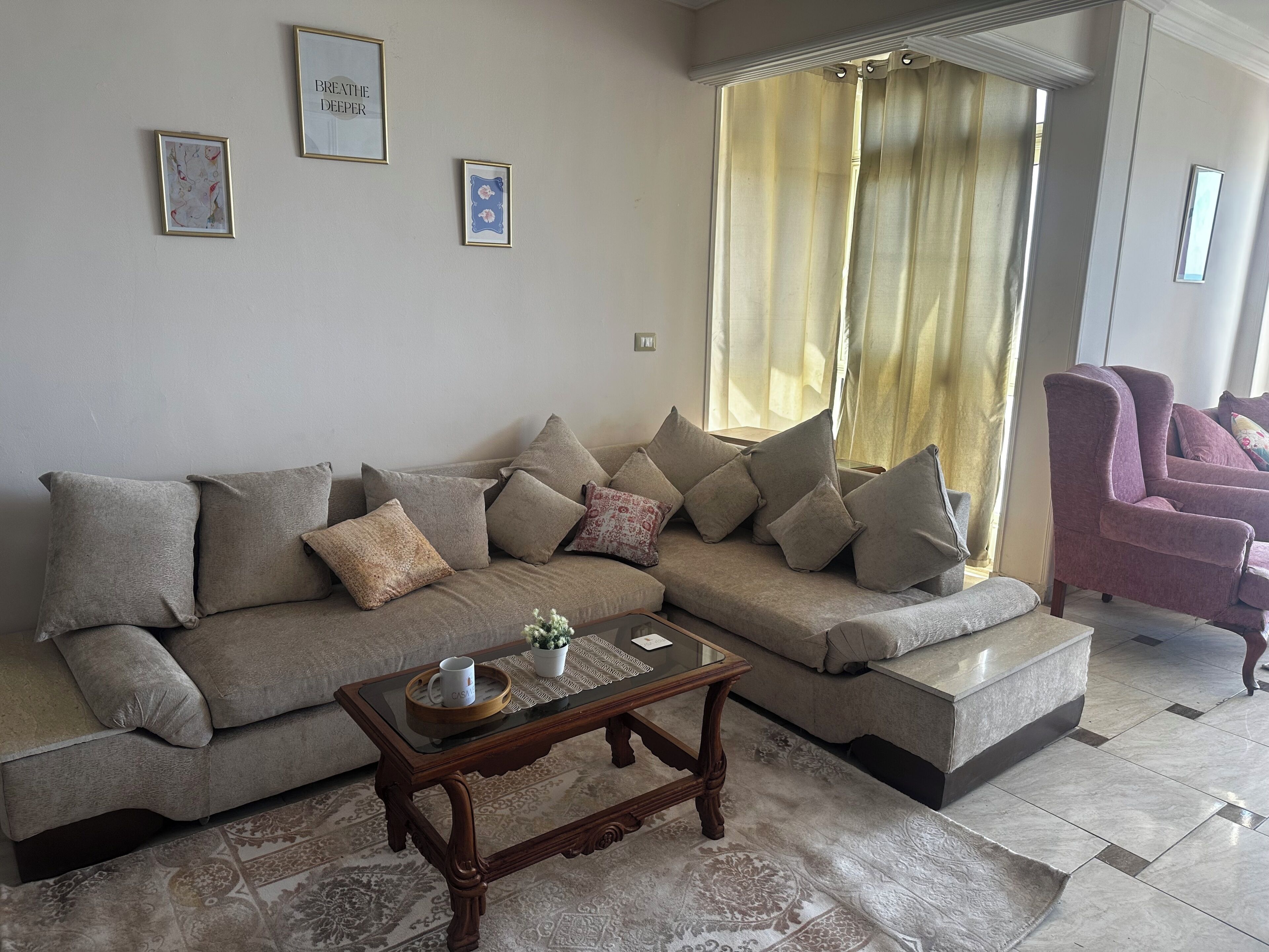 Una sala de estar con un sofá modular, una mesa de centro de vidrio y un sillón púrpura.