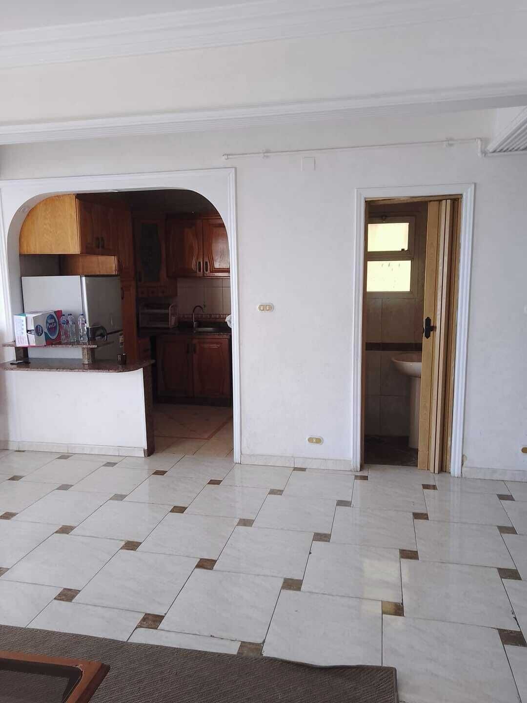 Un espacio habitable amplio con piso de baldosas, una cocina con armarios de madera y un acceso a un baño.