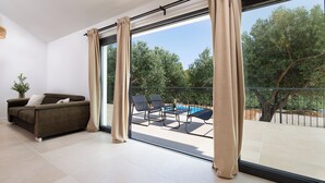 Ein modernes Wohnzimmer mit einer Couch, großen Fenstern und Blick auf einen Pool und Bäume.