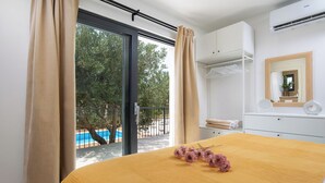 Ein Schlafzimmer mit einem großen Bett, Blick auf einen Swimmingpool und einem Balkon.