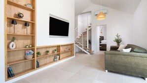 Ein großzügiger Wohnbereich mit einer Holzregal, einem Flachbildfernseher, einer Treppe und einem grünen Sofa.