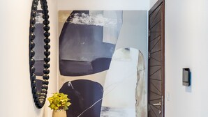 A hallway with a modern abstract painting, a decorative mirror, and a small table with a plant.
