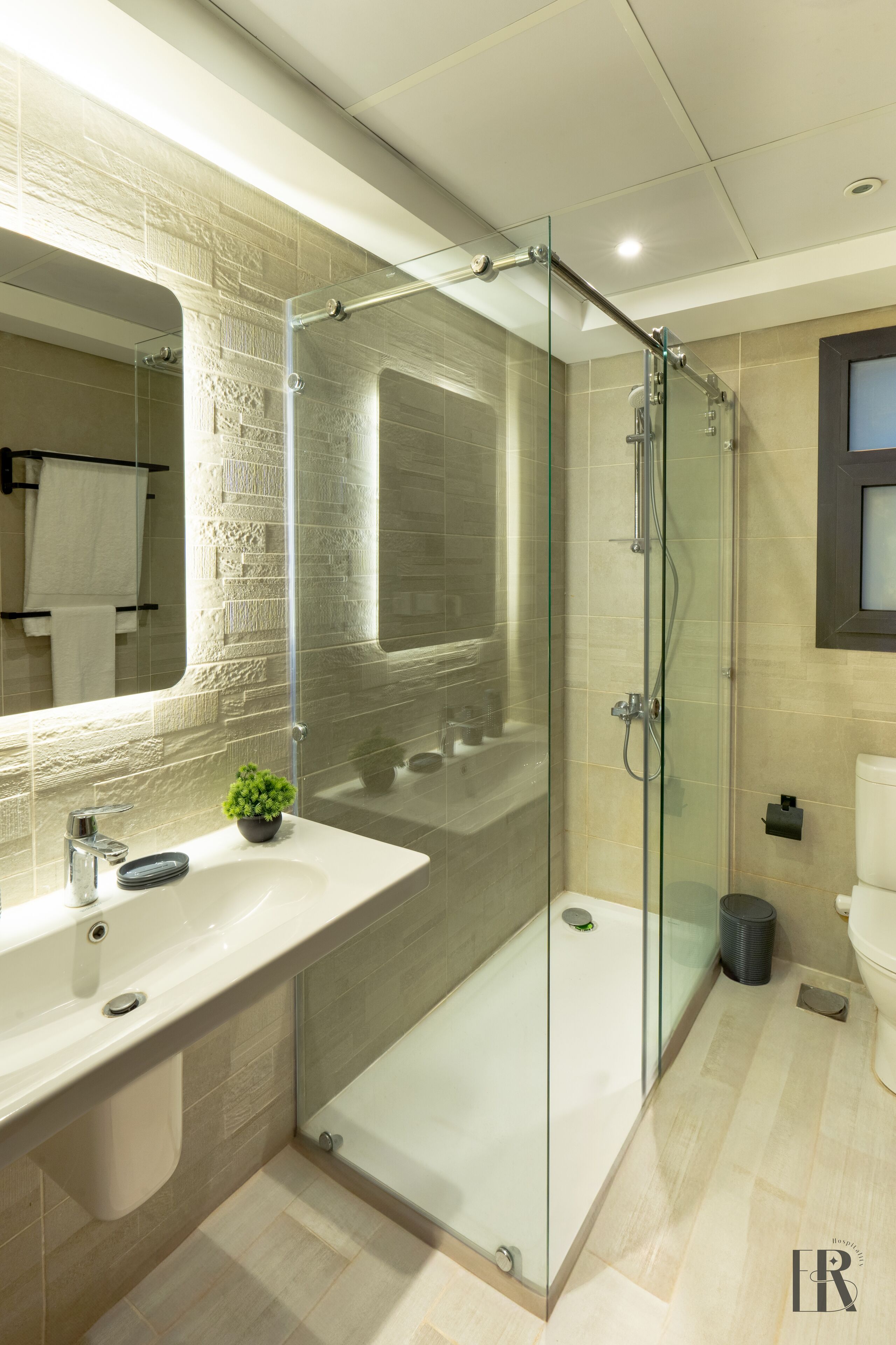 A modern bathroom with a glass-enclosed shower, a large mirror, and a white sink.