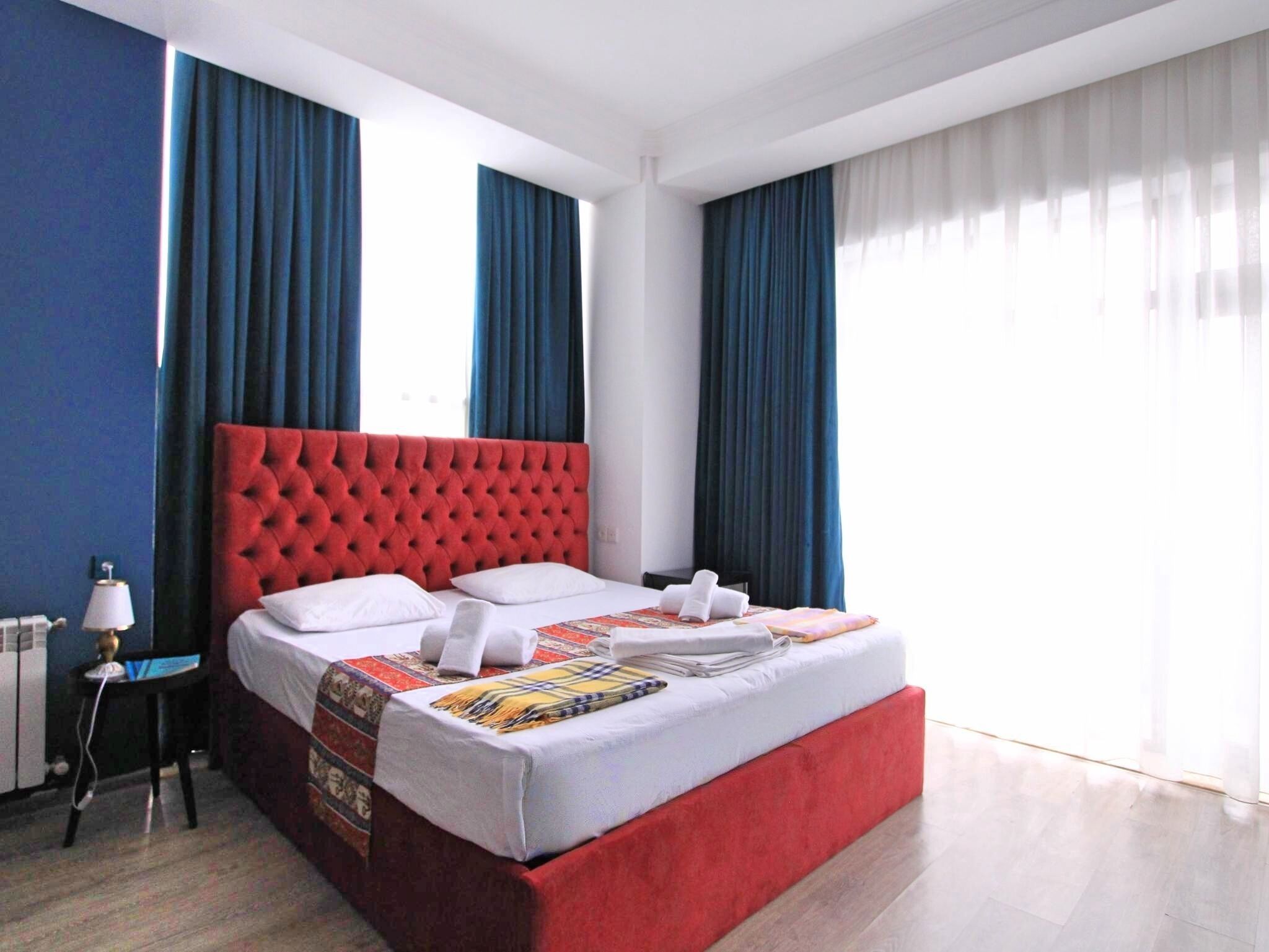 A hotel room with a red tufted headboard, white bedding, and a small table with a lamp.
