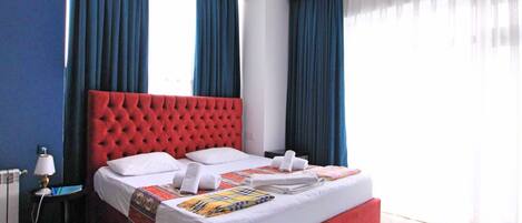 A hotel room with a red tufted headboard, white bedding, and a small table with a lamp.