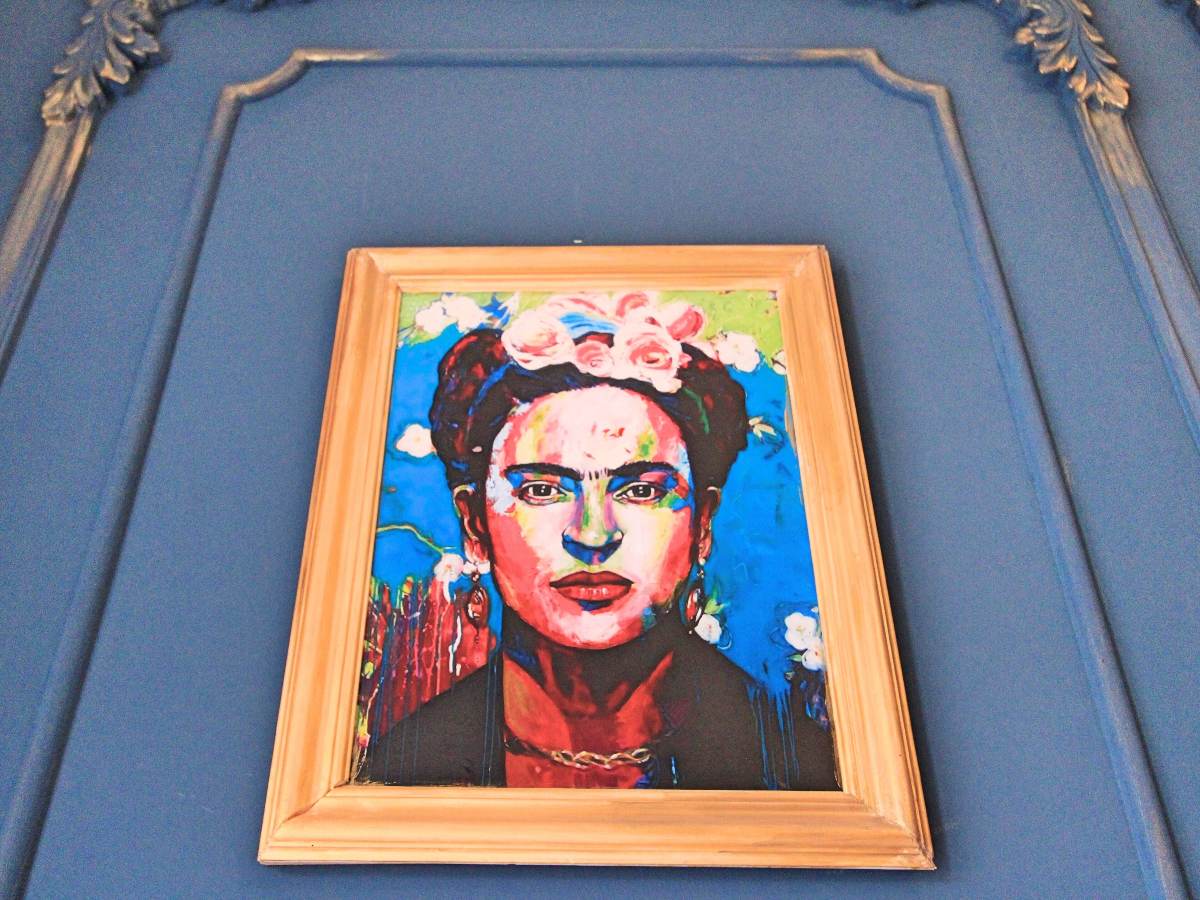 A framed painting on a blue wall with ornate molding.