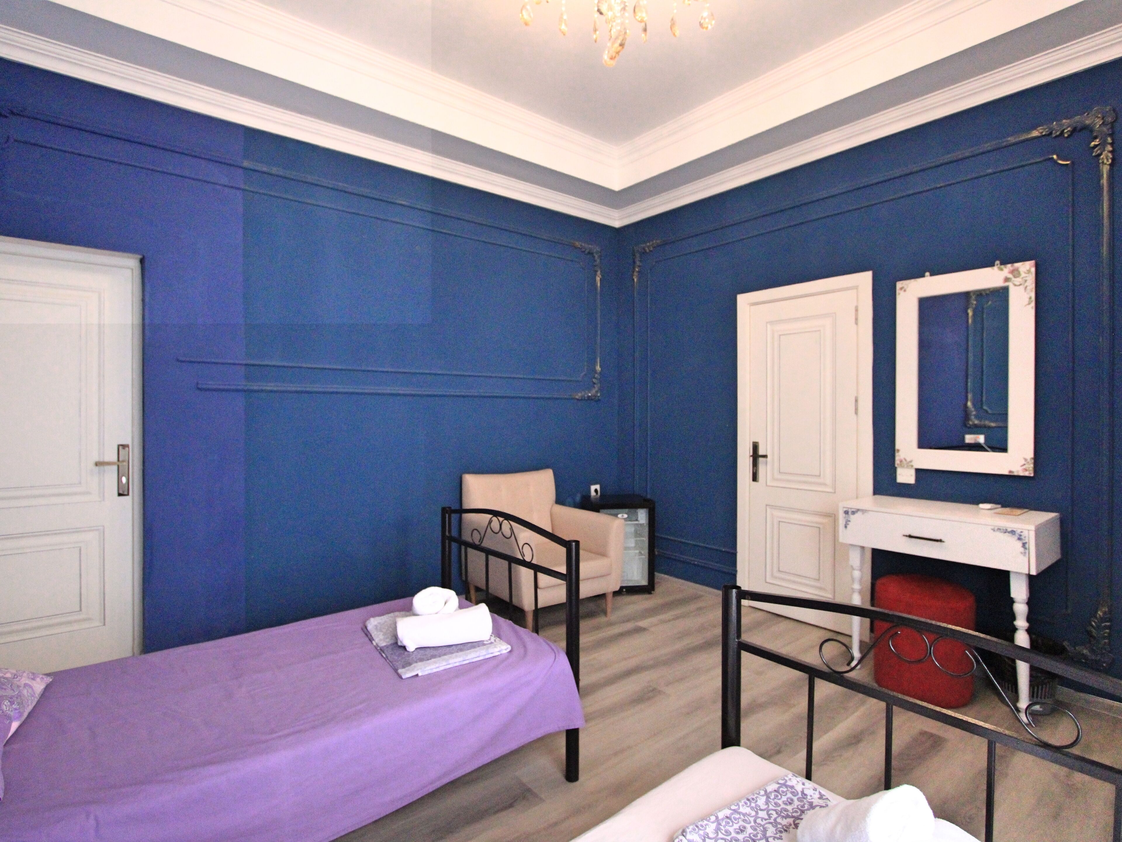 Une chambre avec deux lits, une coiffeuse avec un miroir, un tabouret rouge et une petite table avec une lampe.
