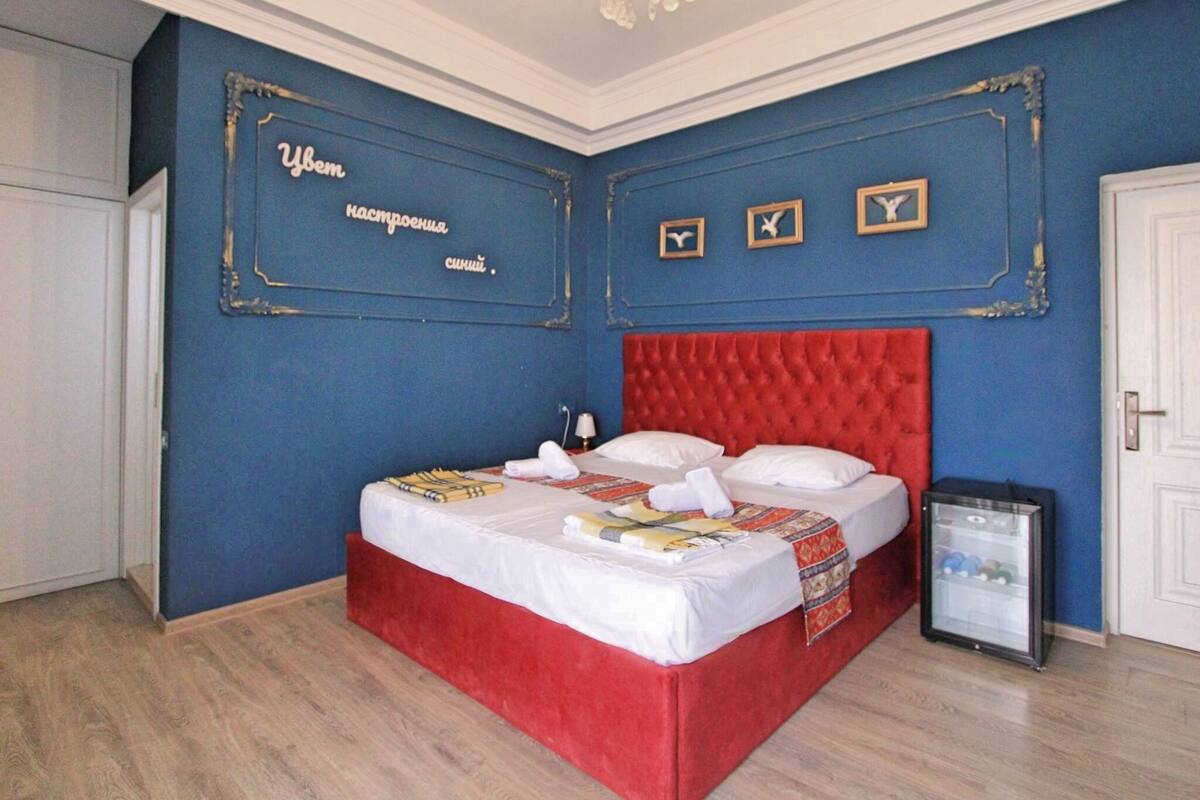 A bedroom with a red upholstered bed, a minibar, and decorative wall art.