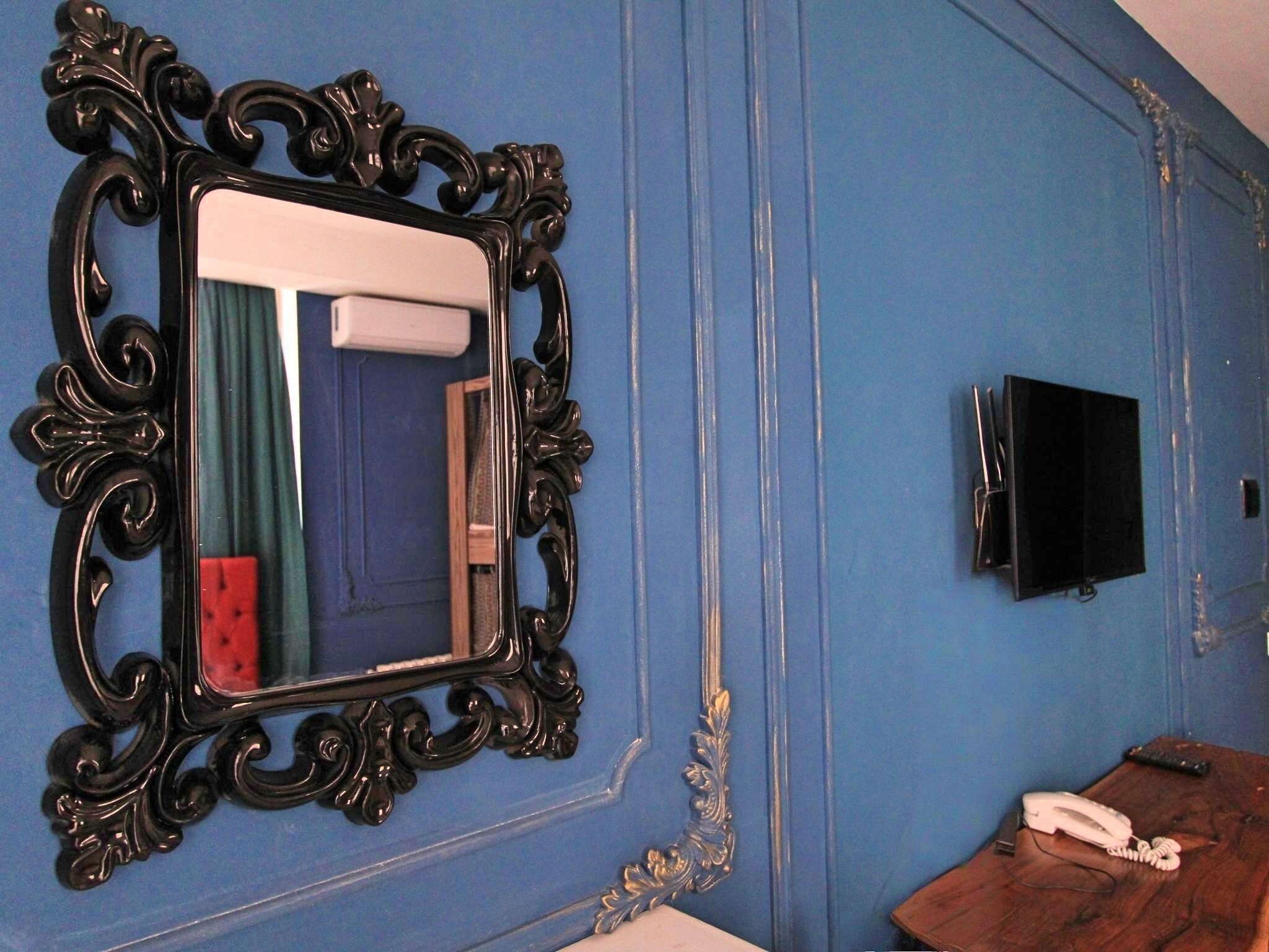 Ein Zimmer mit einem großen, verzierten Spiegel, einem an der Wand montierten Flachbildfernseher und einem Holznachttisch mit Telefon.