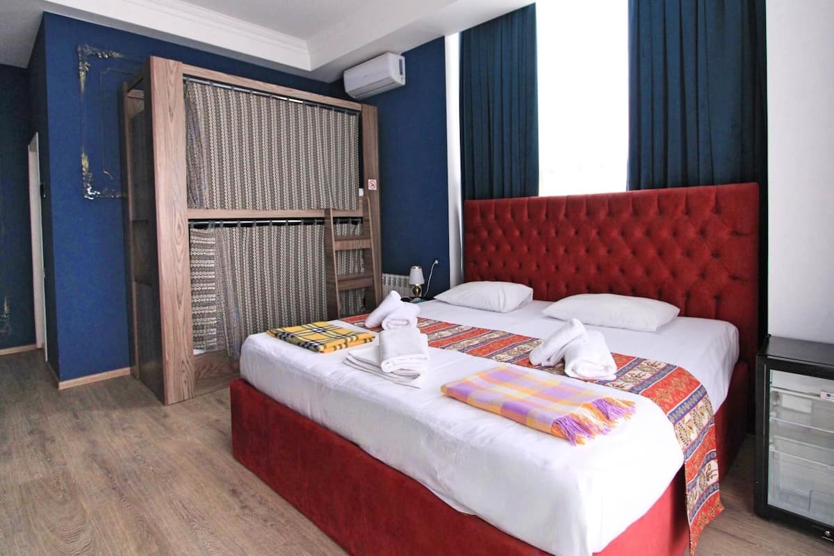 A hotel room with a large bed, a wardrobe, and a small refrigerator.