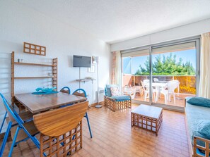 A modern living room with a wooden dining table, blue chairs, a sofa, and a balcony with outdoor furniture.