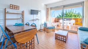 Una sala moderna con una mesa de comedor de madera, sillas azules, un sofá y un balcón con mobiliario exterior.