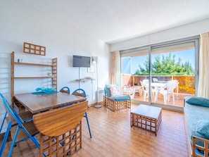 Un salon moderne avec une table à manger en bois, des chaises bleues, un canapé et un balcon aménagé avec du mobilier d’extérieur.