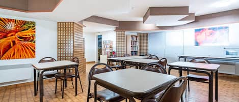 A dining area with tables and chairs, a bookshelf, and a large window.