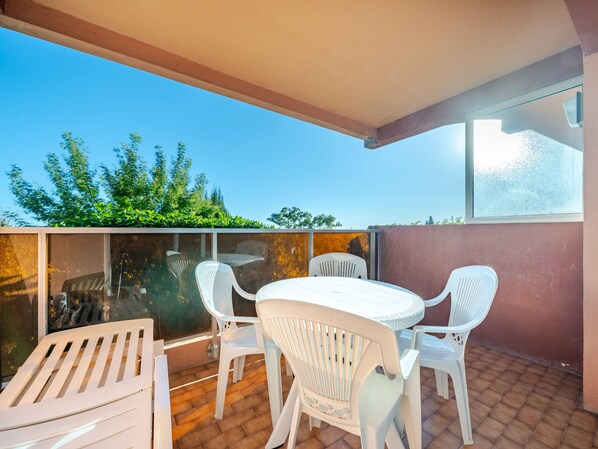 An outdoor patio with a table and chairs, a glass partition, and a view of trees.
