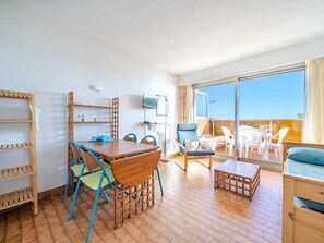 A spacious living area with a wooden dining table, blue chairs, a sofa, and a balcony with white plastic chairs. - Seaside Studio for 4 with Wi-Fi, perfect stay! (Roquebrune-Cap-Martin)