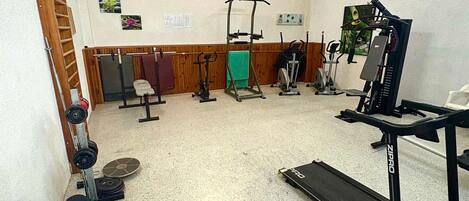 A gym with various exercise equipment including a treadmill, weight bench, and free weights.