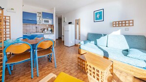 A compact living space with a kitchenette, a dining area with blue chairs, a sofa, and a small wooden table. - Apartment for 6, terrace, Wi-Fi included (Roquebrune-Cap-Martin)