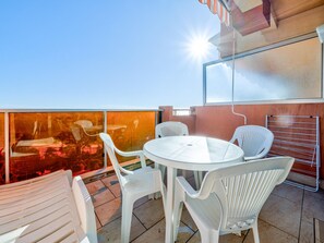 A rooftop terrace with a round glass table and white plastic chairs.
