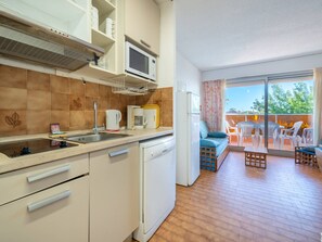 Une cuisine compacte équipée d’un four à micro-ondes, d’une bouilloire et d’une machine à café, ainsi que d’un lave-vaisselle et d’un balcon avec coin salon extérieur.