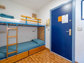 A dormitory room with bunk beds, a wooden ladder, a blue door, and a small window.