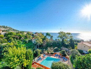 A pool area with lounge chairs, surrounded by greenery and overlooking a coastal landscape.