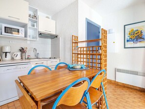 A compact kitchen with white cabinets, a microwave, and a coffee maker. There is a wooden dining table with blue chairs and a basket of bread. - Apartment 6 pers, sea view, Wi-Fi, Roquebrune-Cap-Martin (Roquebrune-Cap-Martin)
