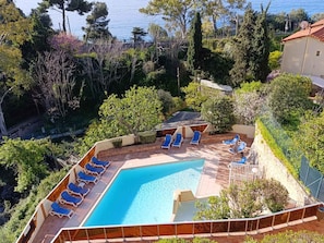 A swimming pool with sun loungers, surrounded by greenery and overlooking a body of water.