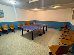 Una mesa de ping pong en una habitación con paredes azules y blancas, rodeada de sillas de madera.