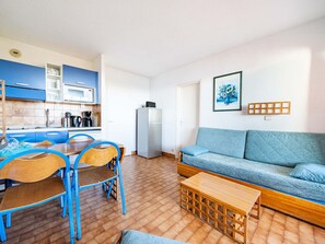 A compact living space with a kitchenette, a dining area with blue chairs, a sofa, and a small wooden table.