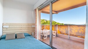 A bedroom with a bed, a wooden headboard, and a balcony with chairs and a table. - Apartment for 8 with equipped kitchenette and Wi-Fi (Roquebrune-Cap-Martin)