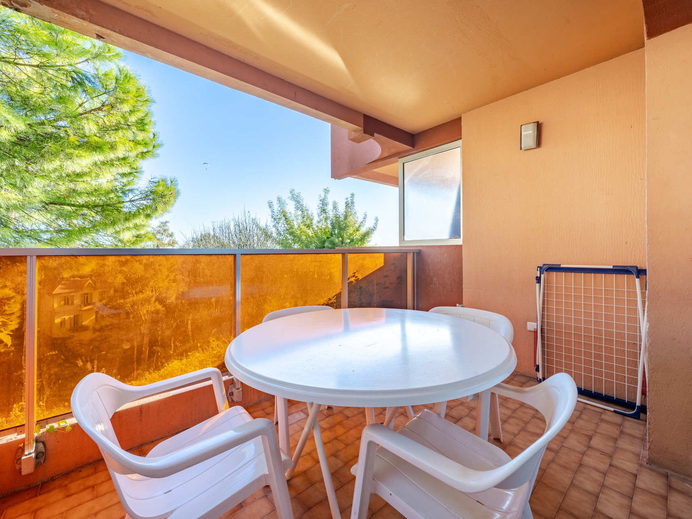 A balcony with a round table and two chairs, a view of trees, and a metal gate.