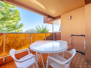 A balcony with a round table and two chairs, a view of trees, and a metal gate.