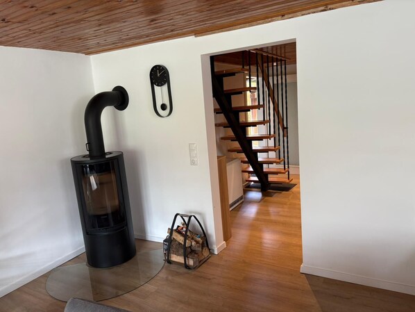 Un interior moderno con una estufa de leña, una escalera y un reloj de pared.