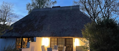 A house with a thatched roof, a patio with chairs, and a small table.