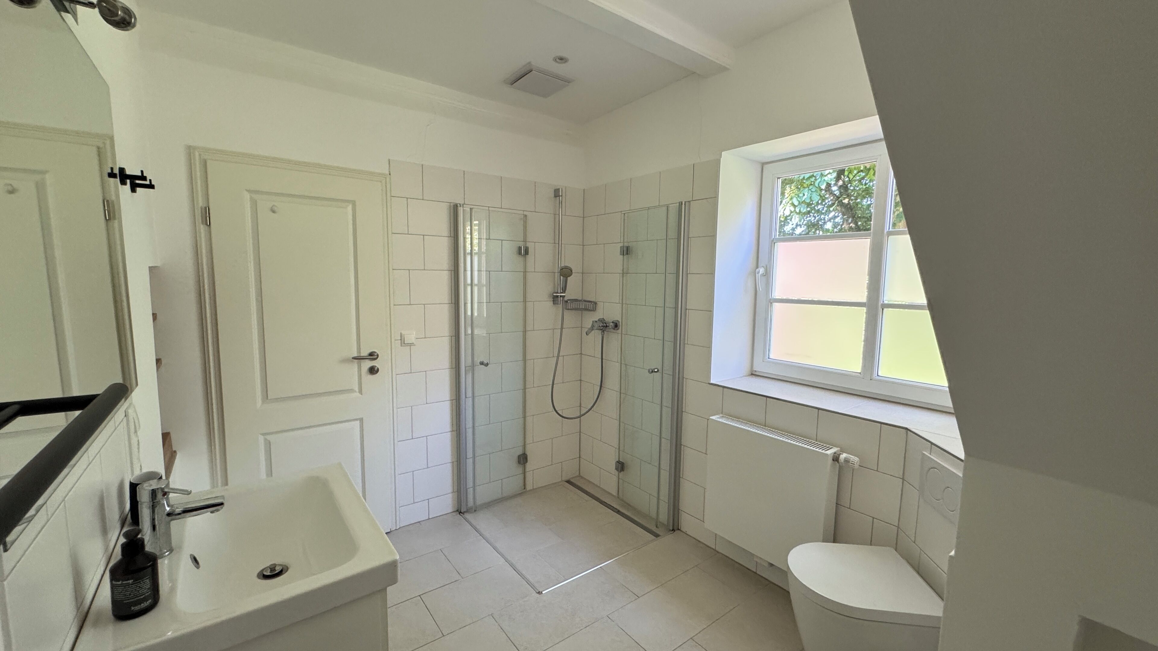 A bathroom with a shower, toilet, sink, and a window providing natural light.
