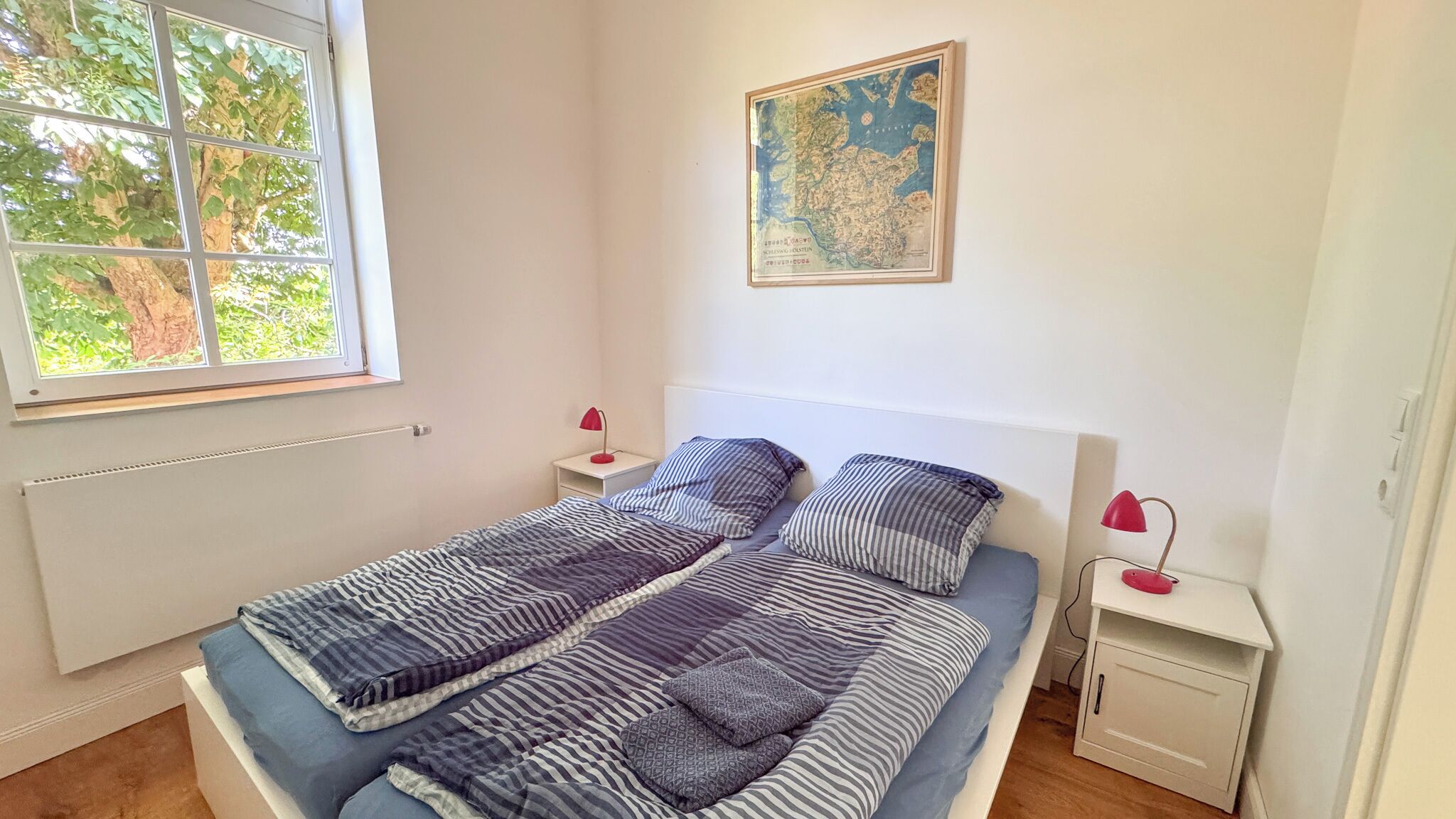 Une chambre à coucher avec un lit, deux tables de chevet, une fenêtre et une carte accrochée au mur.
