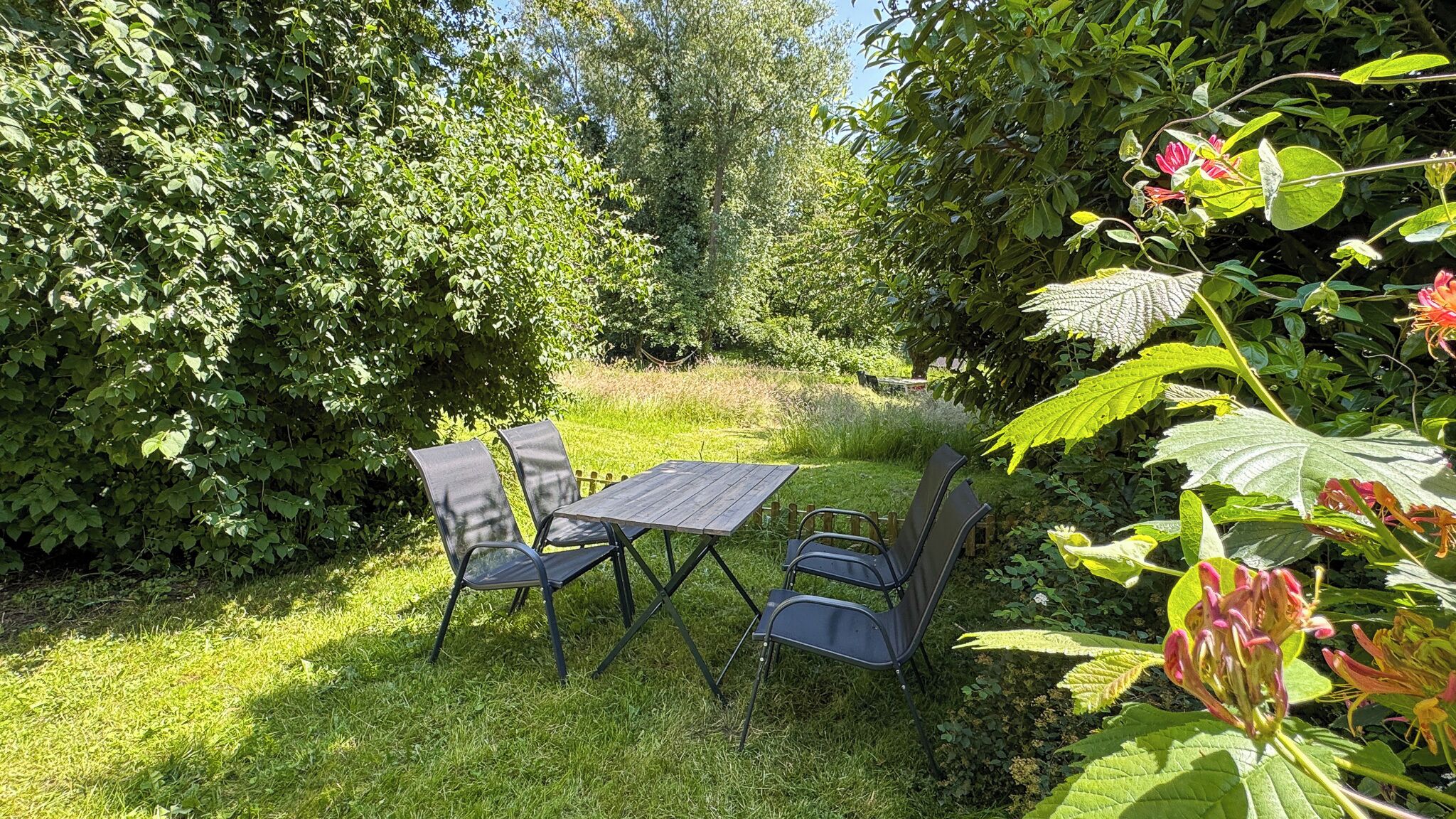 An outdoor seating area with a table and chairs, surrounded by lush greenery and flowering plants.