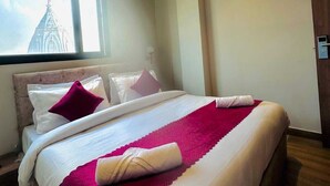 Habitación de hotel con una cama grande, ventilador de techo, equipo de aire acondicionado y ventana con vista a un edificio.