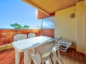 An outdoor balcony with a table and chairs, a view of the sea, and a building with a red and beige facade.