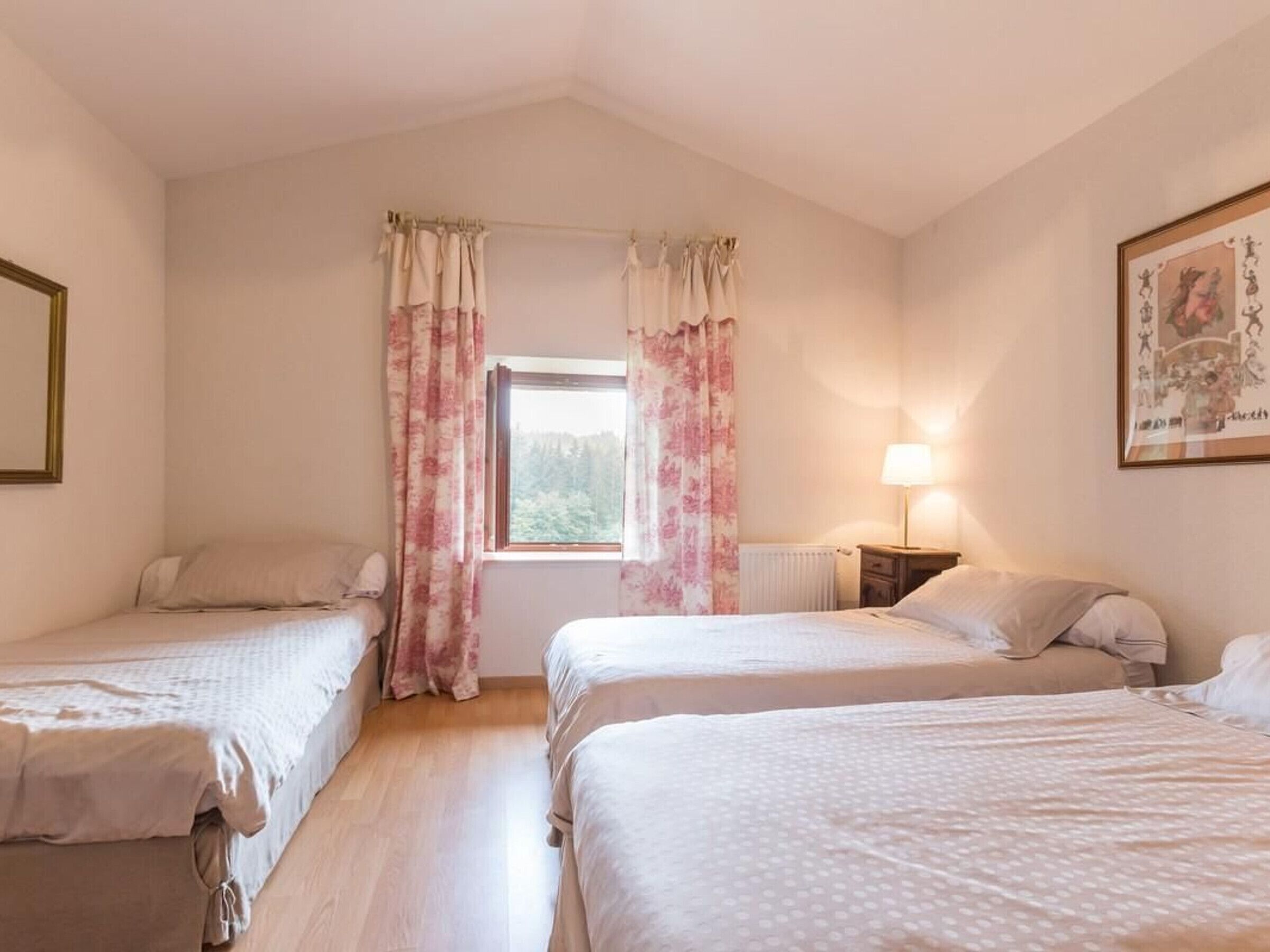 Een slaapkamer met twee eenpersoonsbedden, een raam met gordijnen, een bedlampje en een lijst met een afbeelding aan de muur.