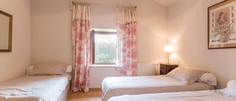 Een slaapkamer met twee eenpersoonsbedden, een raam met gordijnen, een bedlampje en een lijst met een afbeelding aan de muur.