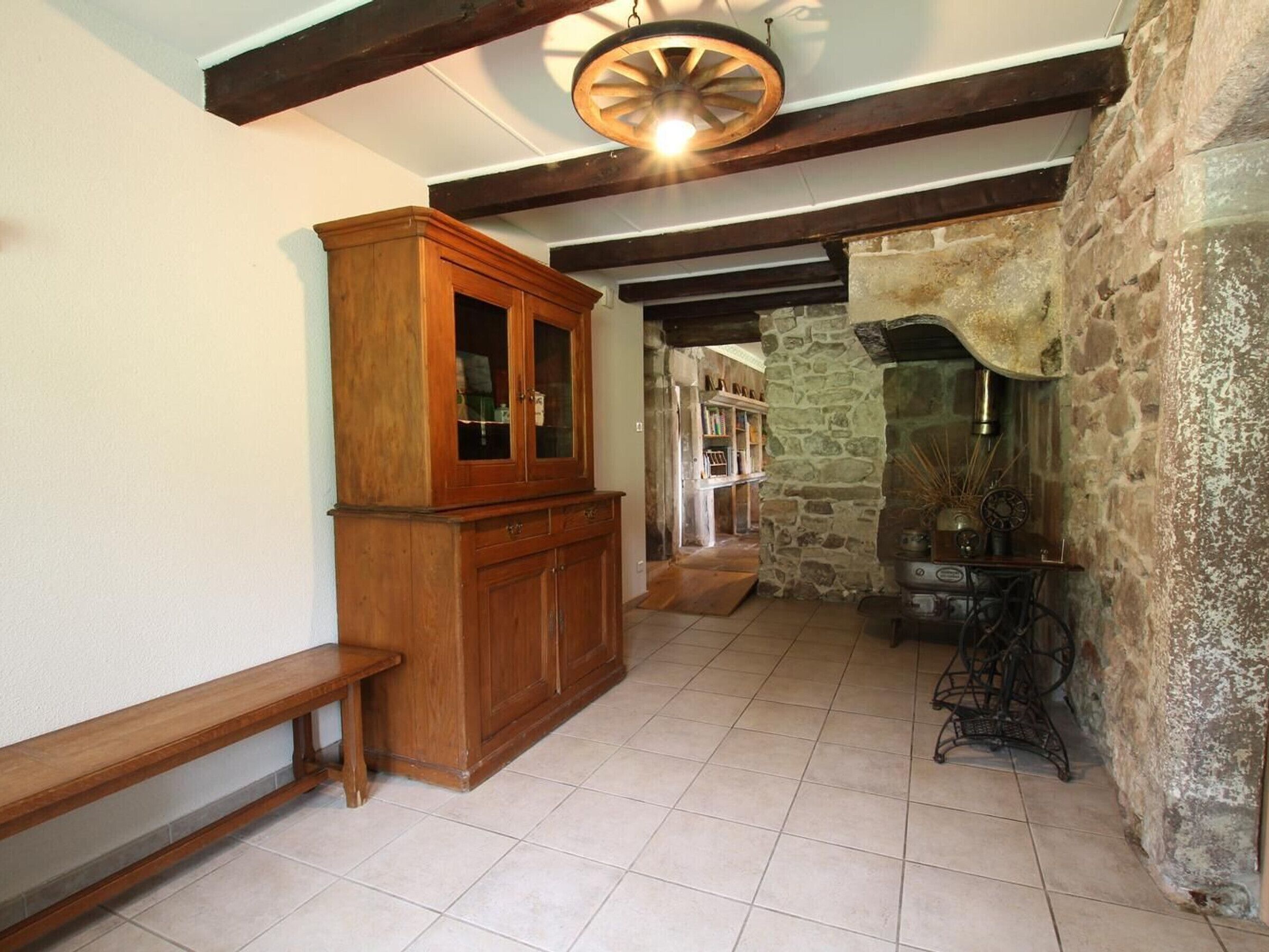 Un interior rústico con paredes de piedra vista, un aparador de madera, un banco y una máquina de coser antigua.