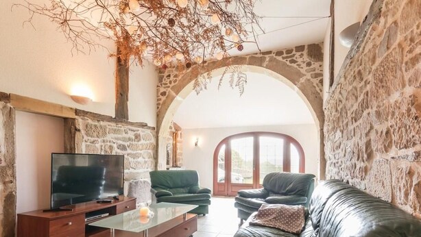 Una sala de estar con pared de piedra, televisor, mesa de centro de vidrio y sofá de cuero.