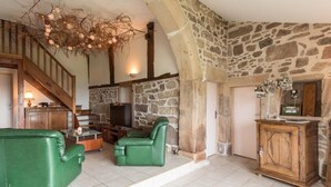 Una sala de estar rústica con paredes de piedra, una escalera de madera, sofás de cuero verde y una chimenea.