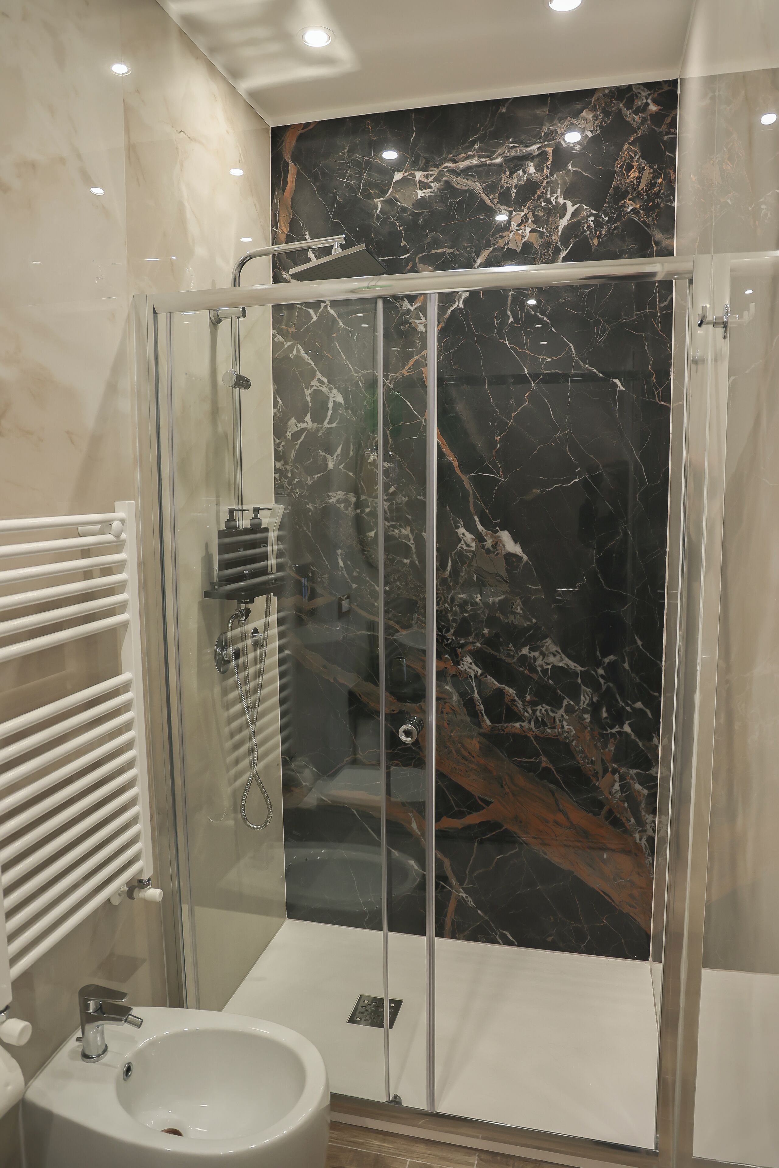 A modern bathroom with a glass-enclosed shower, a white sink, and a marble wall.
